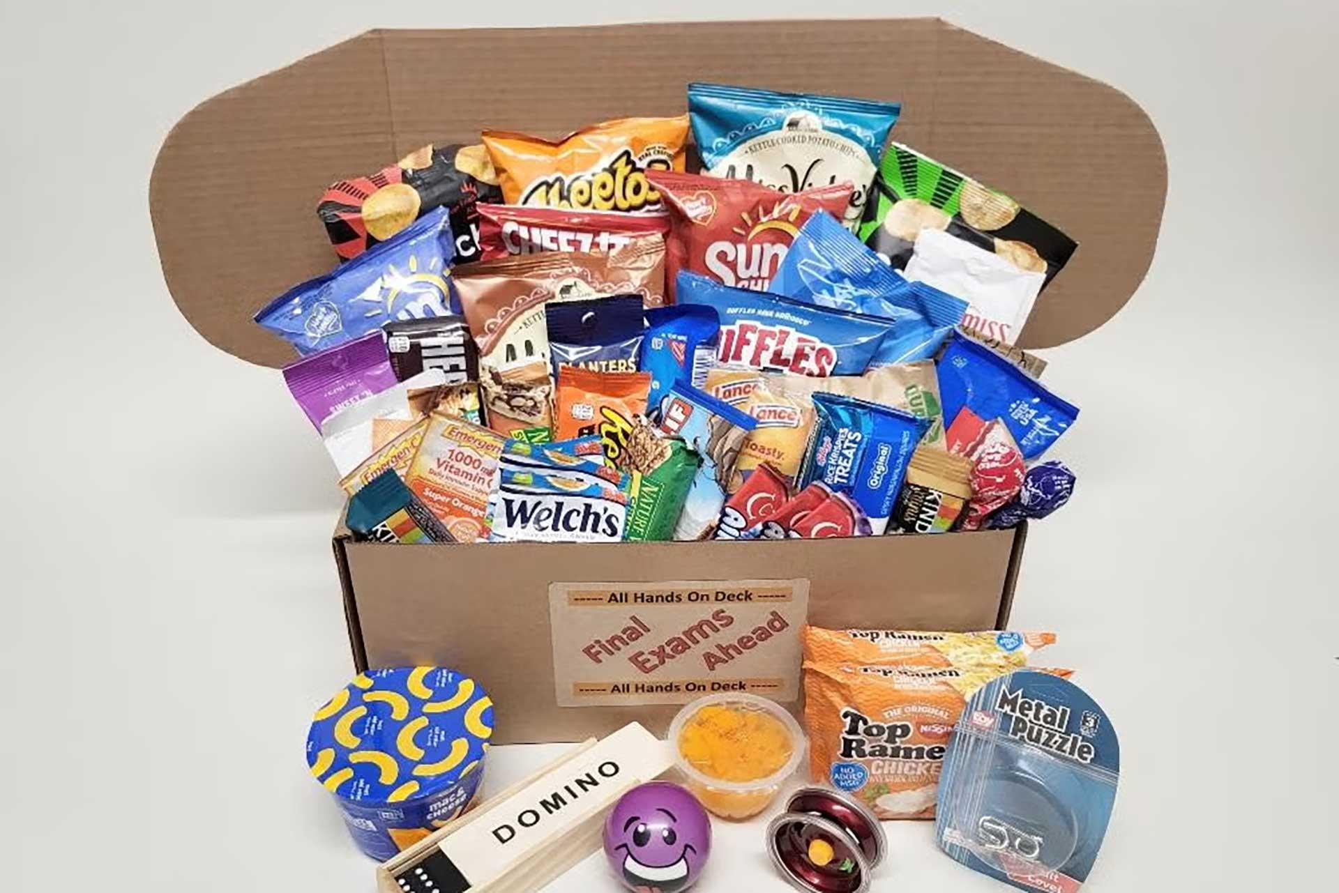 Open cardboard box overflowing with snack bags, ramen, fidget toys, and more.